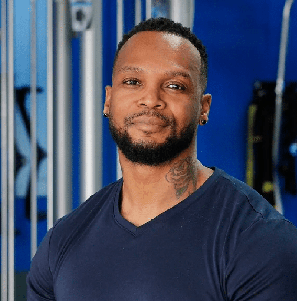 A man with tattoos is standing in front of some blue walls.
